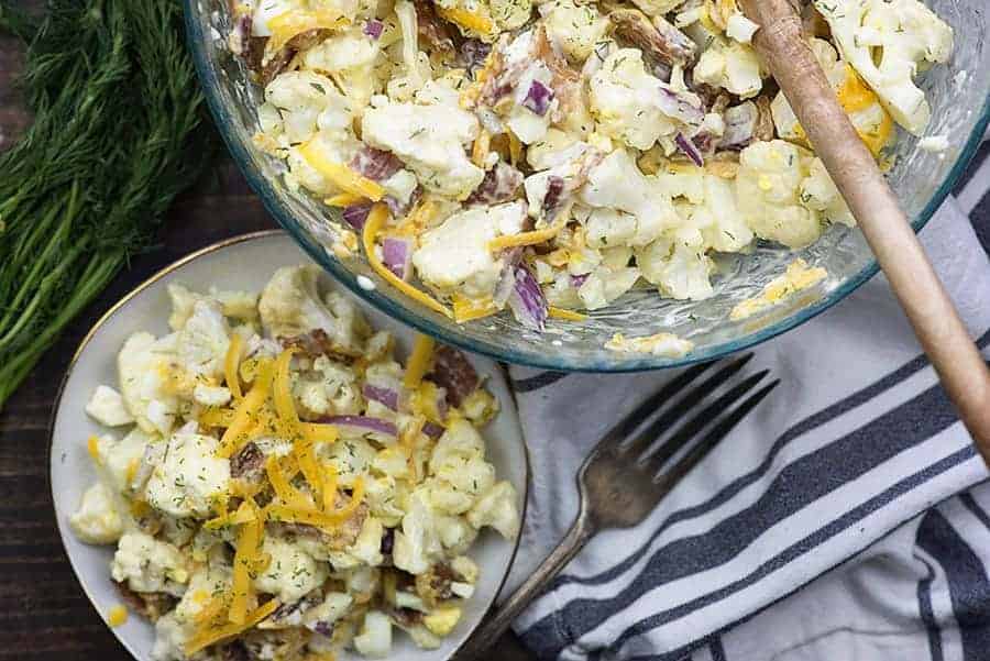 Cauliflower potato salad on white plate next to glass bowl of pasta salad.