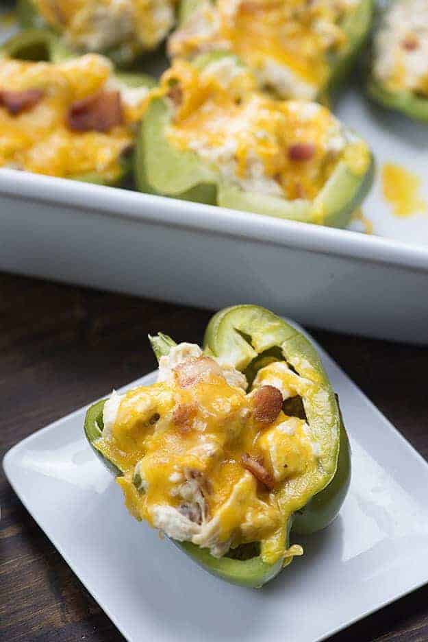 A stuffed pepper on a small white plate with a pan of peppers in the background.