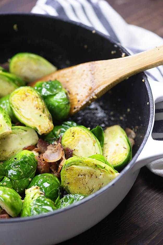 brussels sprouts in white skillet with wooden spoon