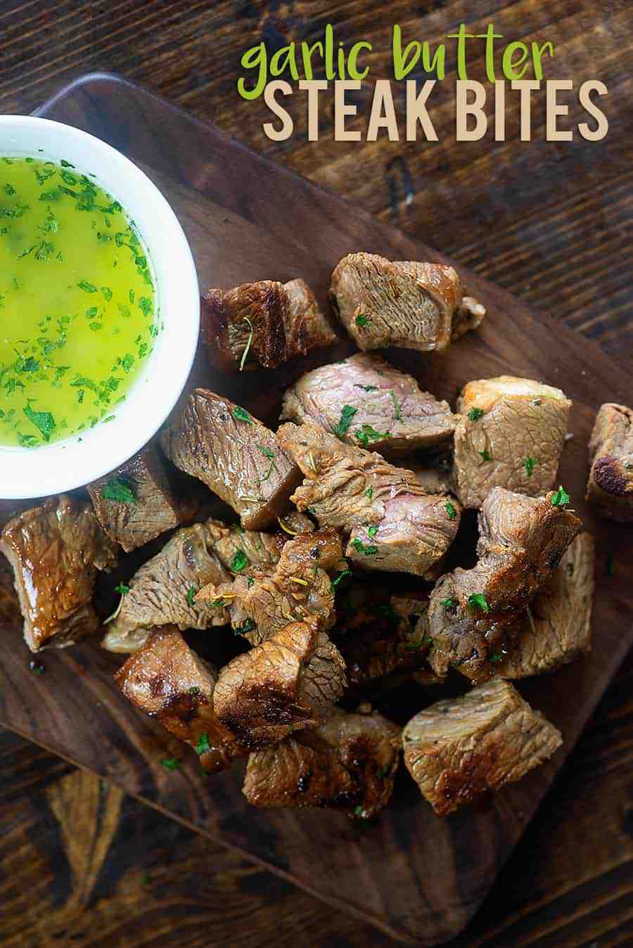Steak bites cut up on a wooden plate with a cup of garlic butter.
