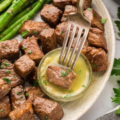 Steak bite being dipped in garlic butter sauce on plate next to asparagus.