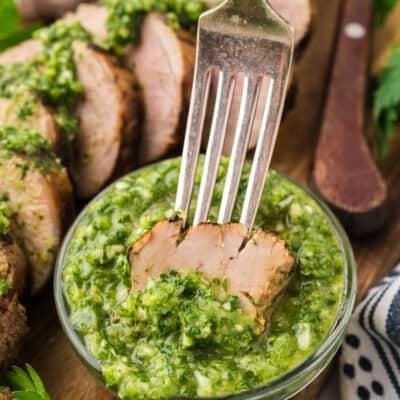 Pork tenderloin piece being dipped in homemade cilantro chimichurri.