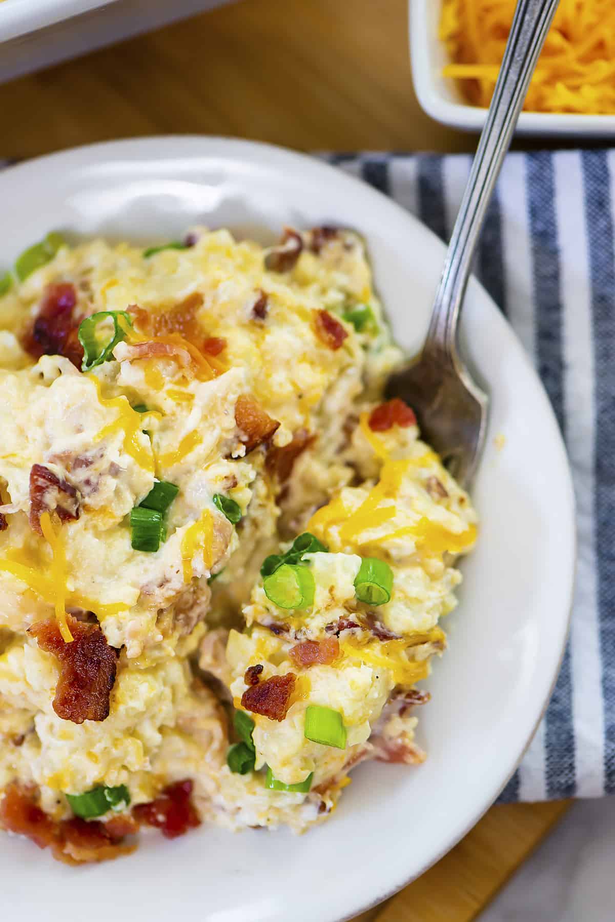 Loaded cauliflower casserole on small white plate.