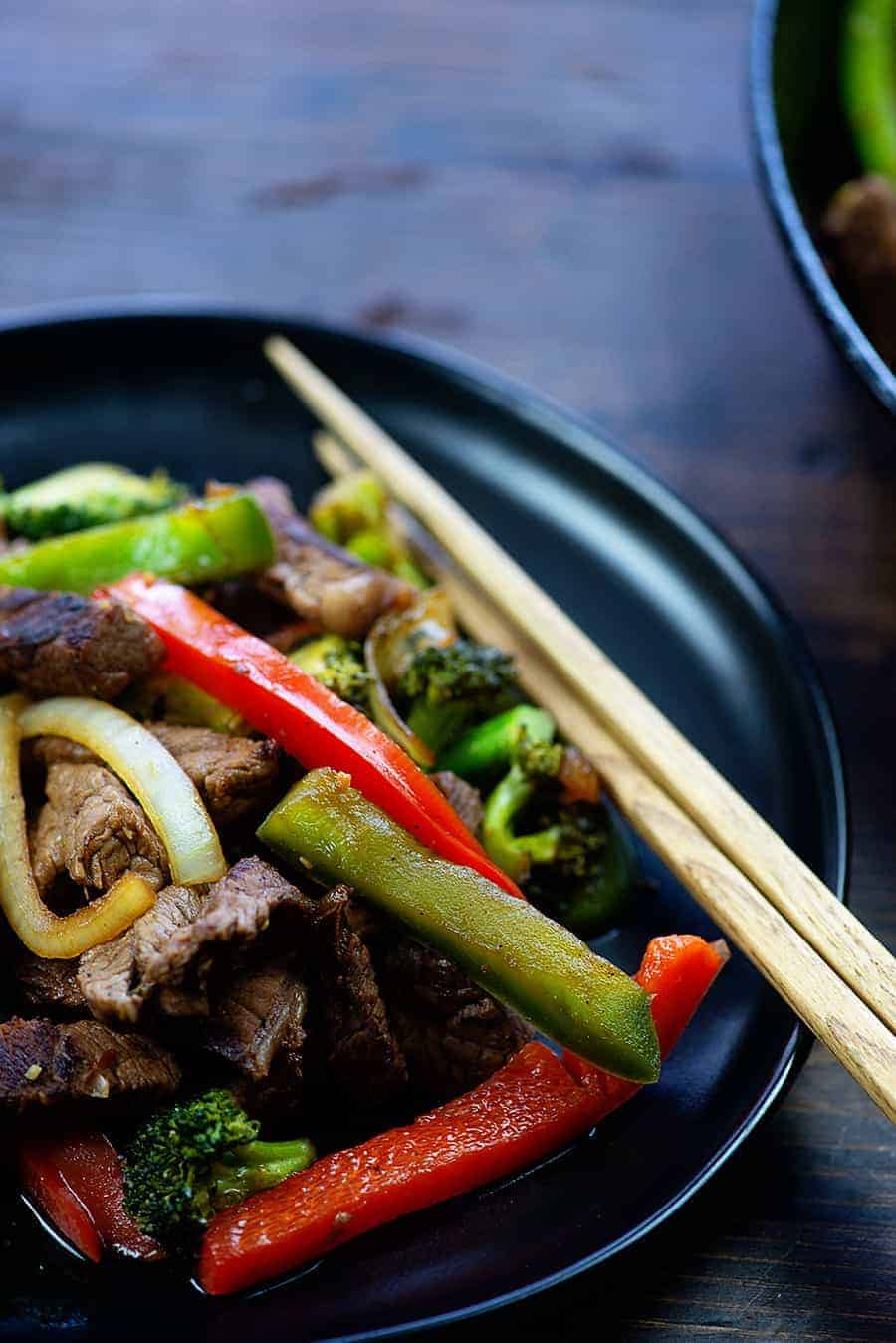 Stir fry on a black plate with chopsticks.