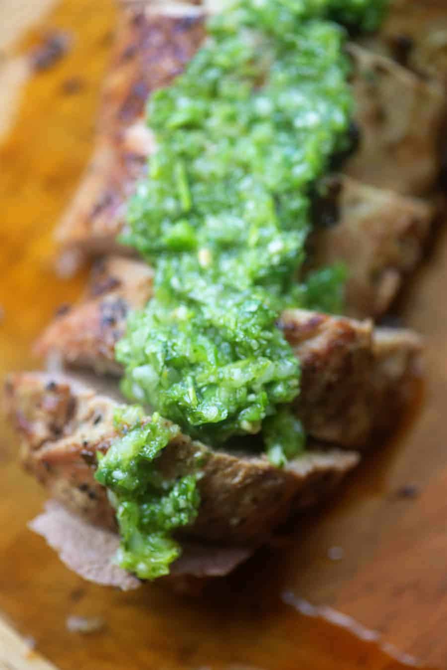 Cut pork tenderloin with chimichurri sauce on top.