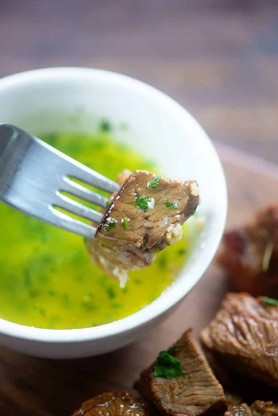 Steak on a fork being dipped in a cup garlic butter steak sauce 