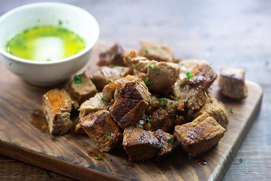 Steak bites on cutting board with a cup of garlic butter.