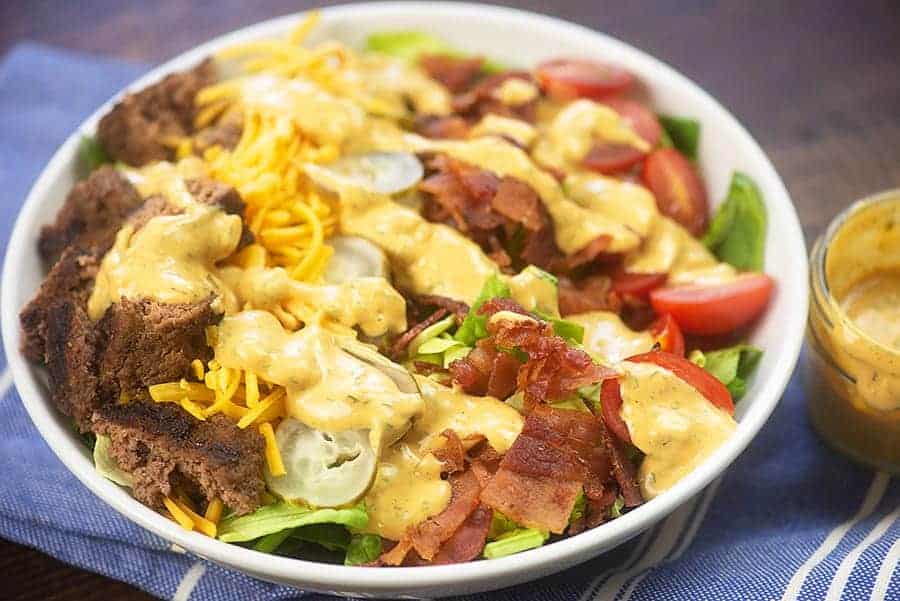 cheeseburger salad in white bowl with jar of dip on side.