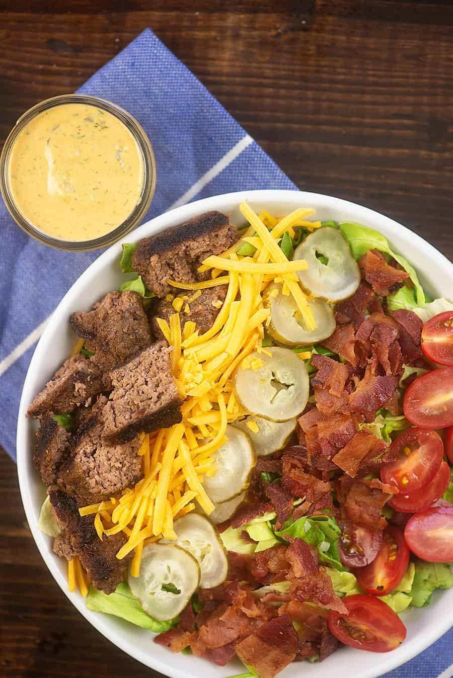 Cheeseburger salad ingredients separated in bowl with jar of burger sauce