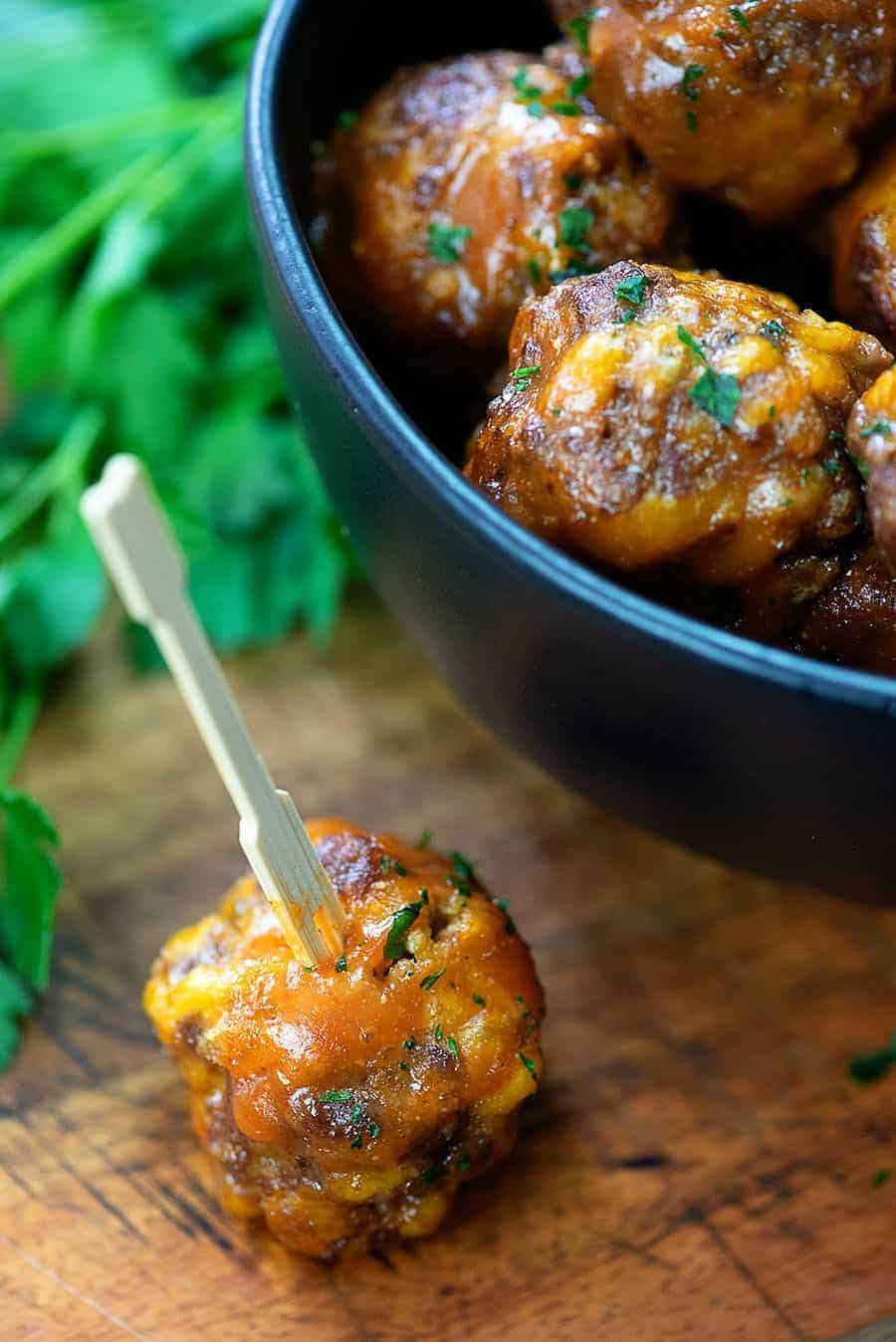 BBQ meatball on a cutting board next to a bowl of meatballs