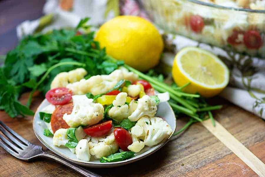 cauliflower salad with greens, lemon, and fork on a small white plate.