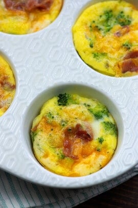 white Muffin Tin containing a few cookedFrittata with bacon, cheddar, and broccoli