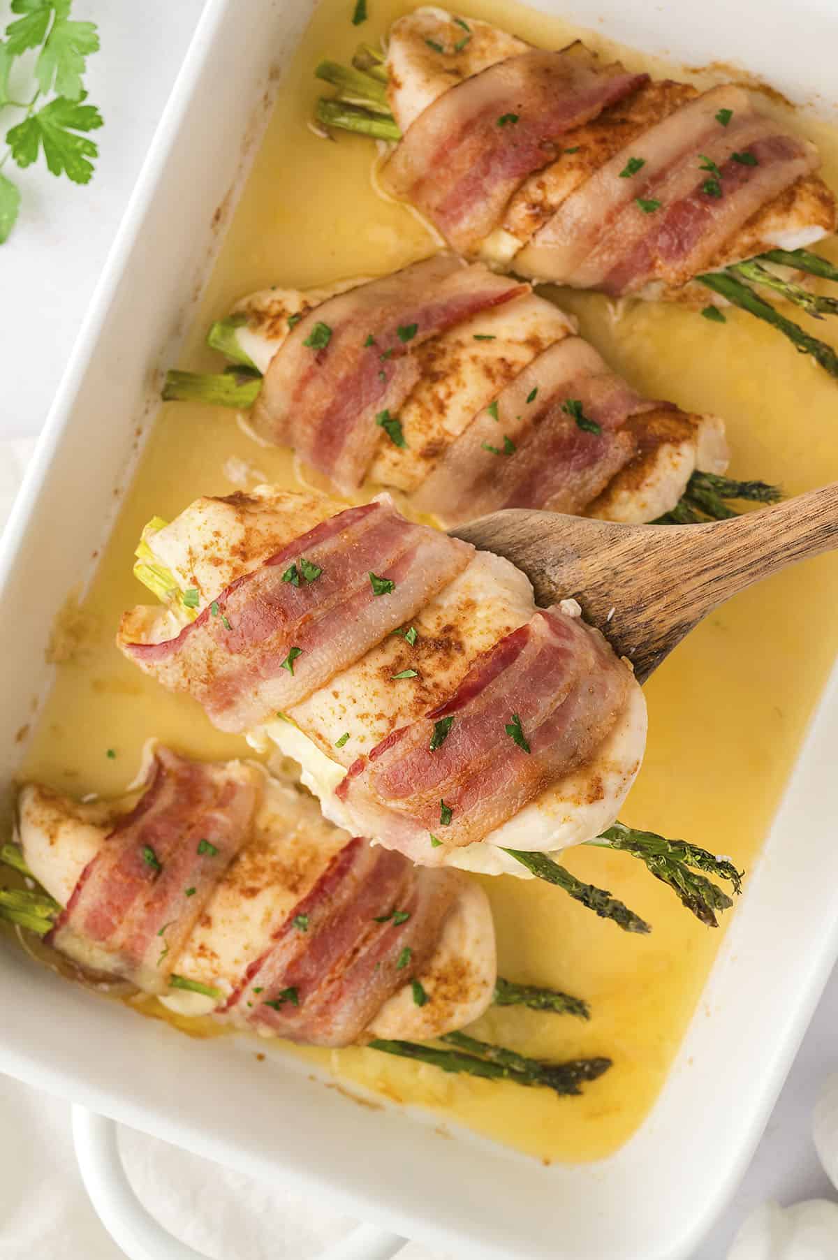 chicken stuffed with asparagus and wrapped in bacon in white baking dish