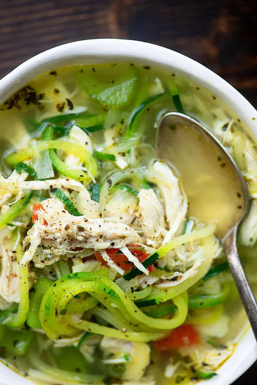 bowl full of chicken zoodle soup with a spoon dipping in