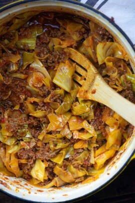 cabbage and sausage in a dutch oven with a wooden spoon stirring it
