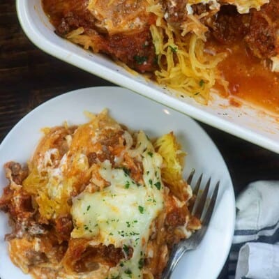 Overhead view of spaghetti squash in a baking dish next to a plate with a serving on it.