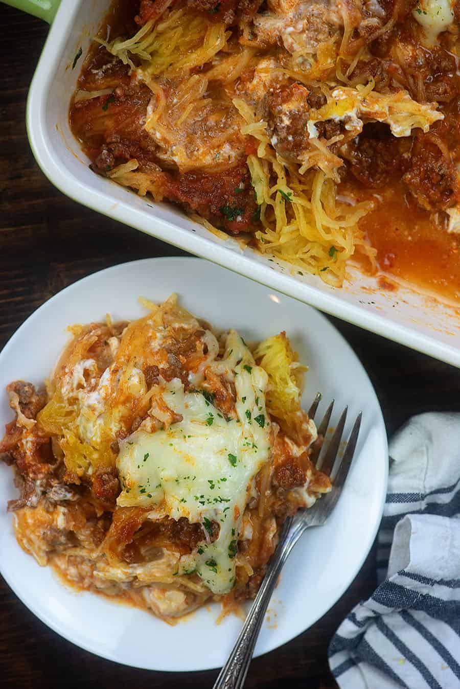 Overhead view of spaghetti squash in a baking dish next to a plate with a serving on it.