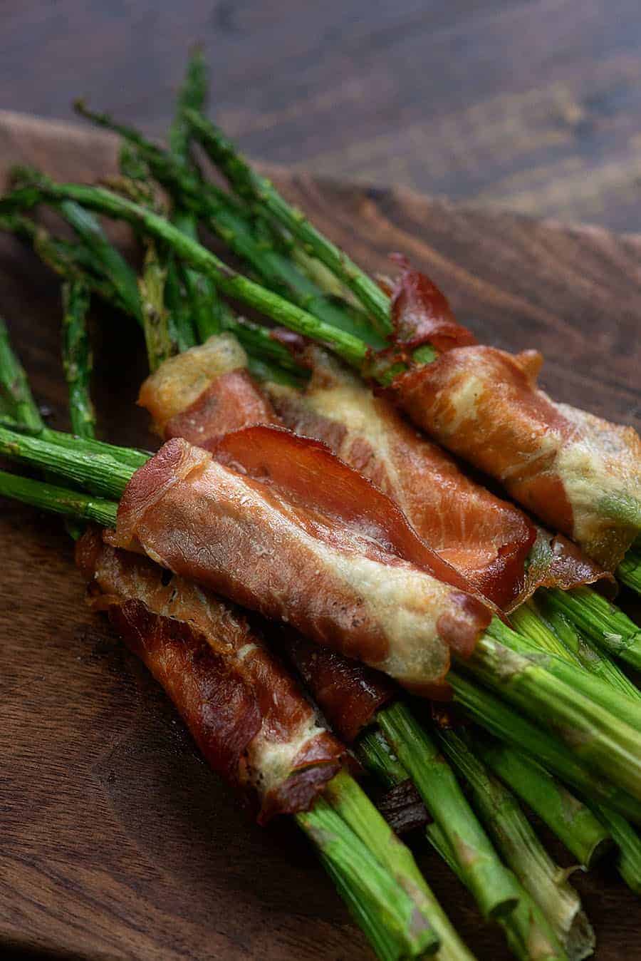 Cooked bacon wrapped asparagus on a cutting board.