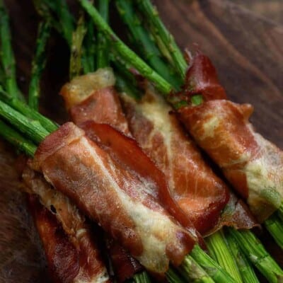 several asparagus each wrapped in prosciutto on top of a dark cutting board