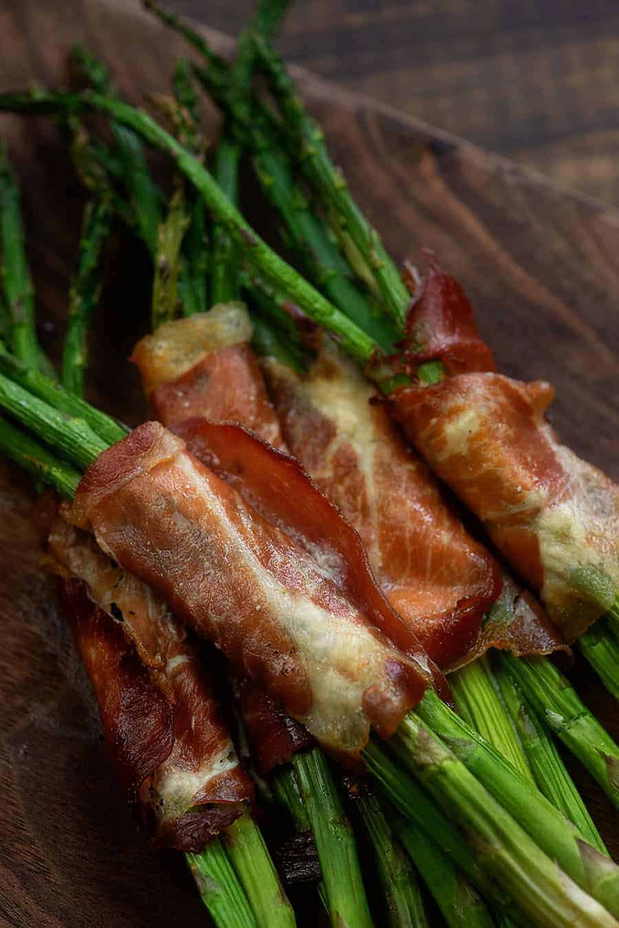several asparagus each wrapped in prosciutto on top of a dark cutting board