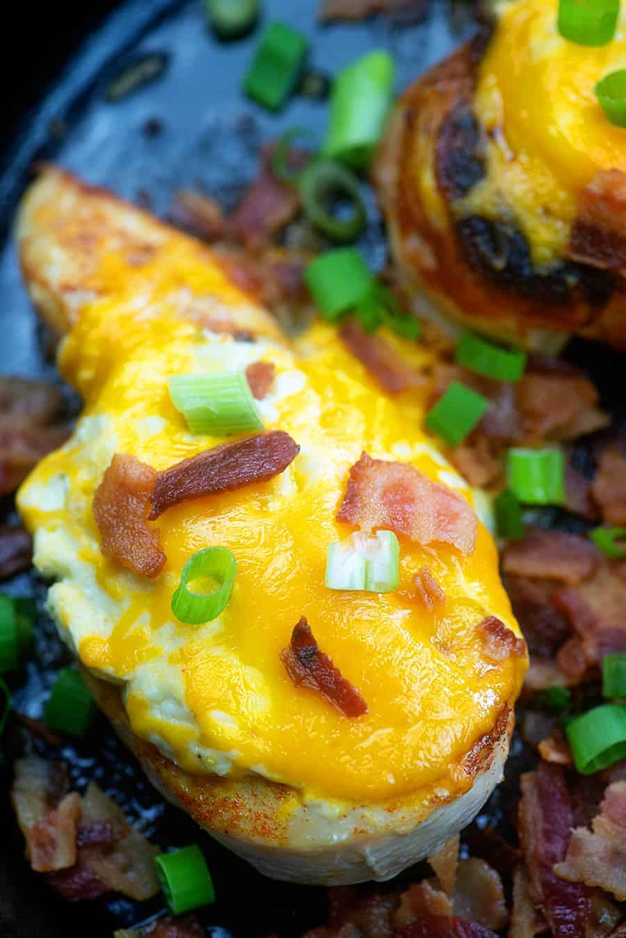 An overhead view of chicken breast topped with cheddar, bacon, and green onions.