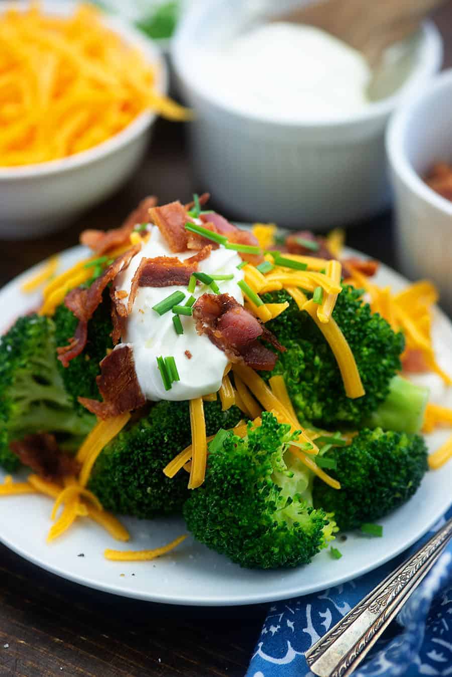 Plate full of broccoli topped with cheese, bacon, and sour cream.