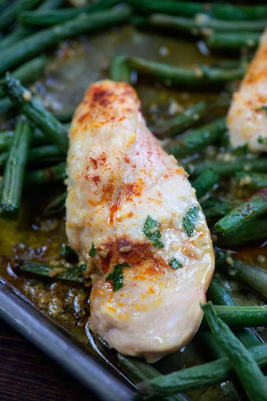 chicken breast on green beans in a cookie sheet