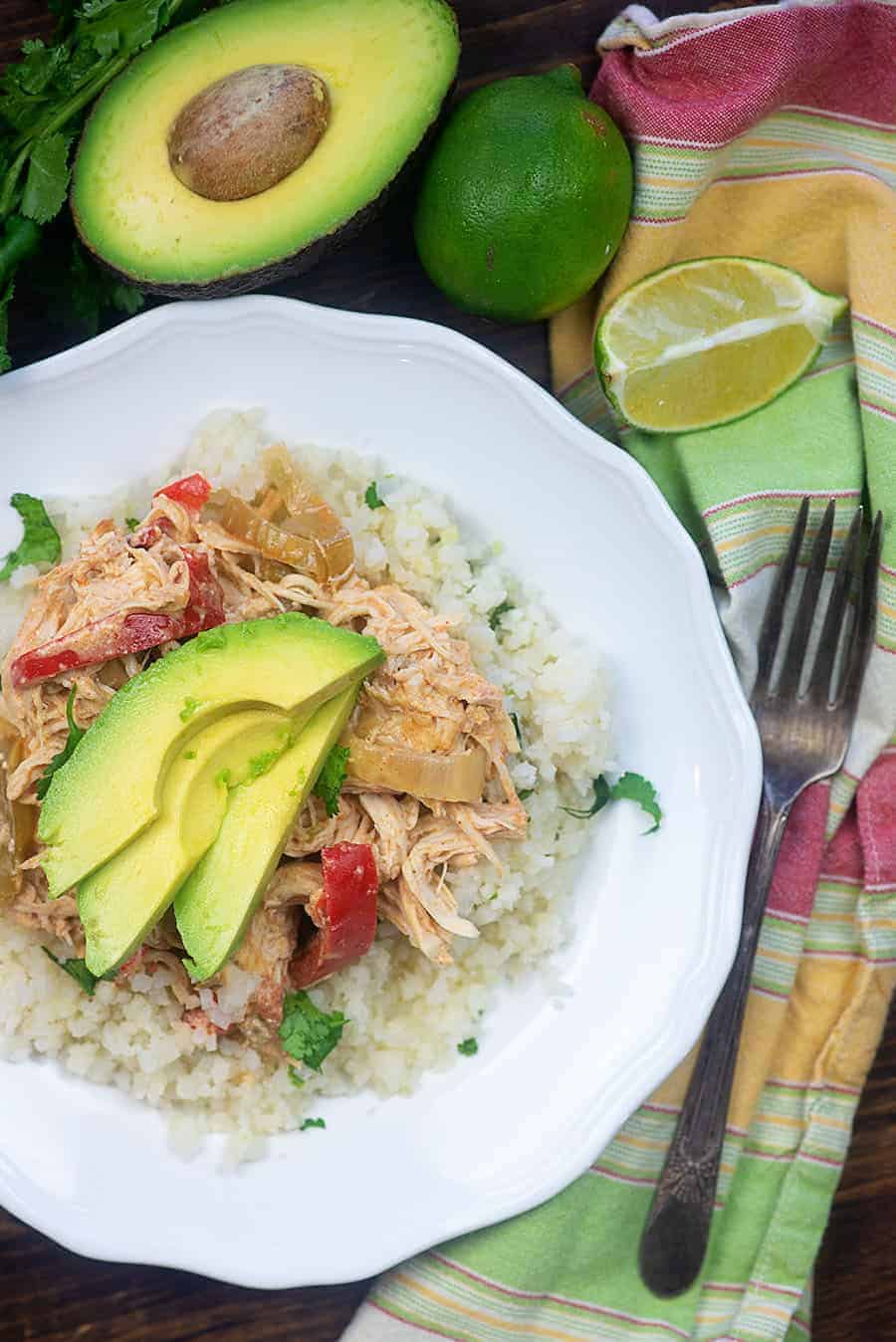 chicken fajitas topped with avocado slices on a white plate with colorful cloth napkin