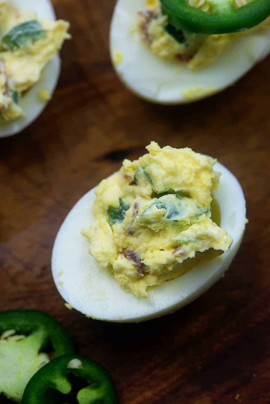 single deviled egg on a cutting board with sliced jalepenos