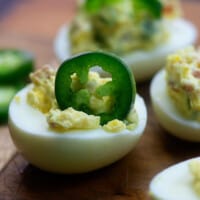 deviled eggs on a cutting board with a sliced jalepeno sticking straight up out of one of the eggs