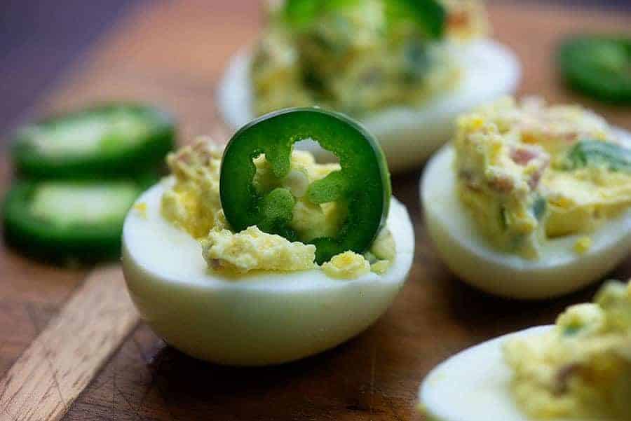 deviled eggs on a cutting board with a standing sliced jalapeno on an egg