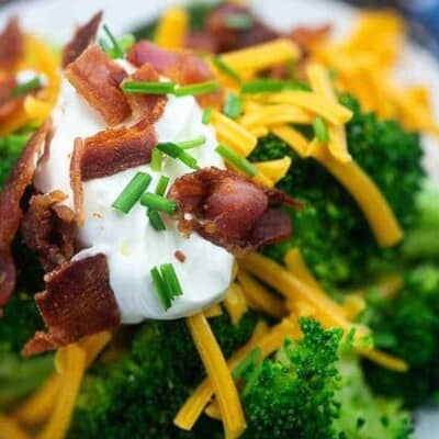 Steamed broccoli on a plate topped with shredded cheese, sour cream, and broccoli