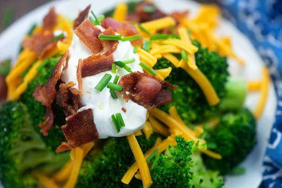 Steamed broccoli on a plate topped with shredded cheese, sour cream, and broccoli