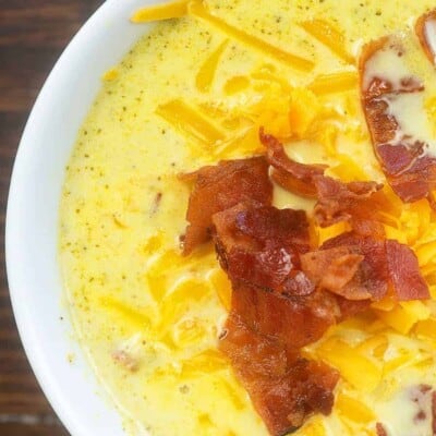 A close up of broccoli soup topped with bacon and shredded cheese.