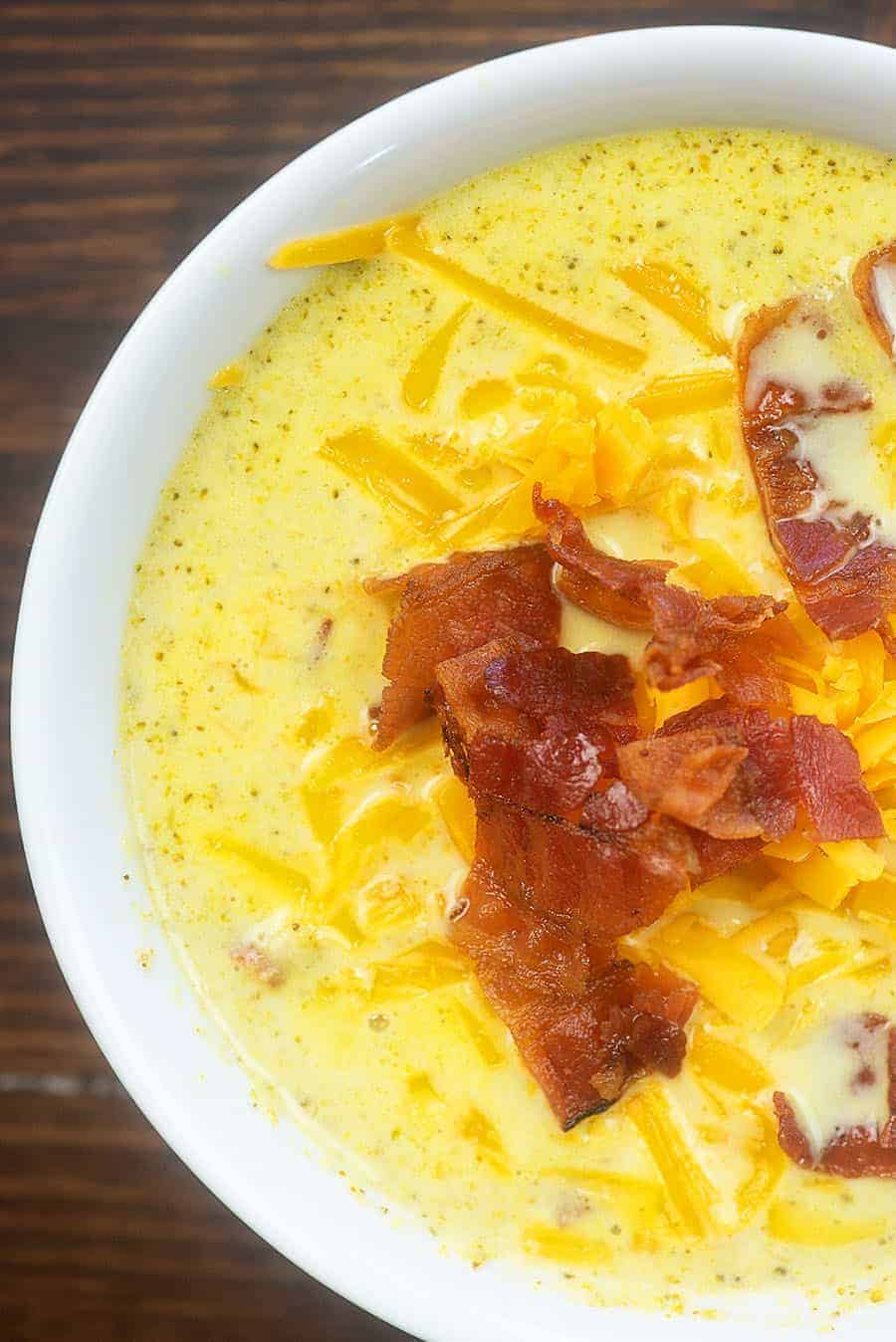 A close up of broccoli soup topped with bacon and shredded cheese.