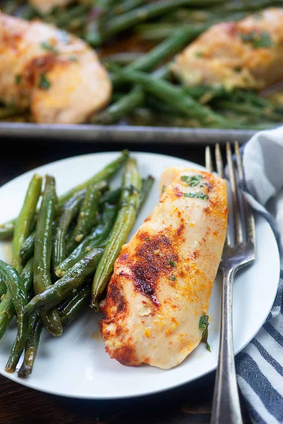 chicken and green beans on a white plate with fork and dish towel