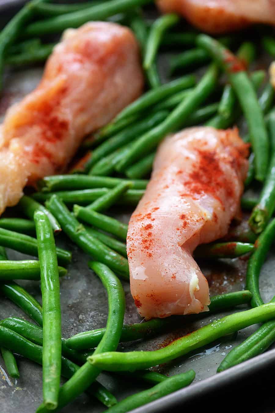 raw chicken and green beans spread out in a baking sheet