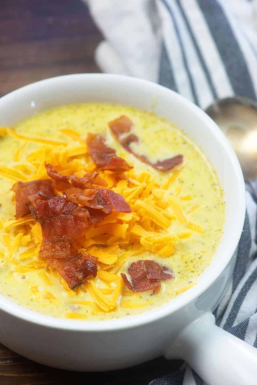 A white bowl of broccoli soup topped with bacon.