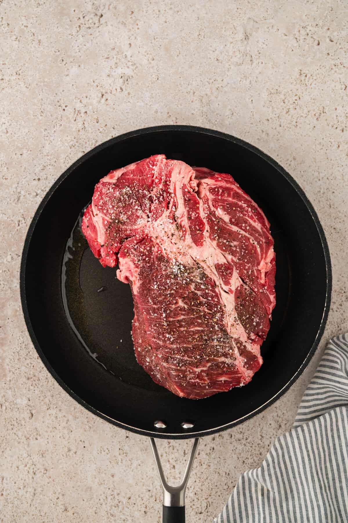 Seasoned chuck roast being seared in skillet.