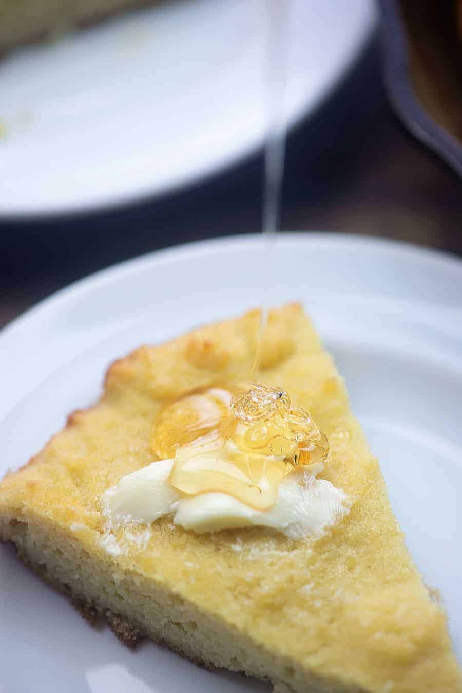 A close up of a piece of cornbread getting honey poured on top of it.