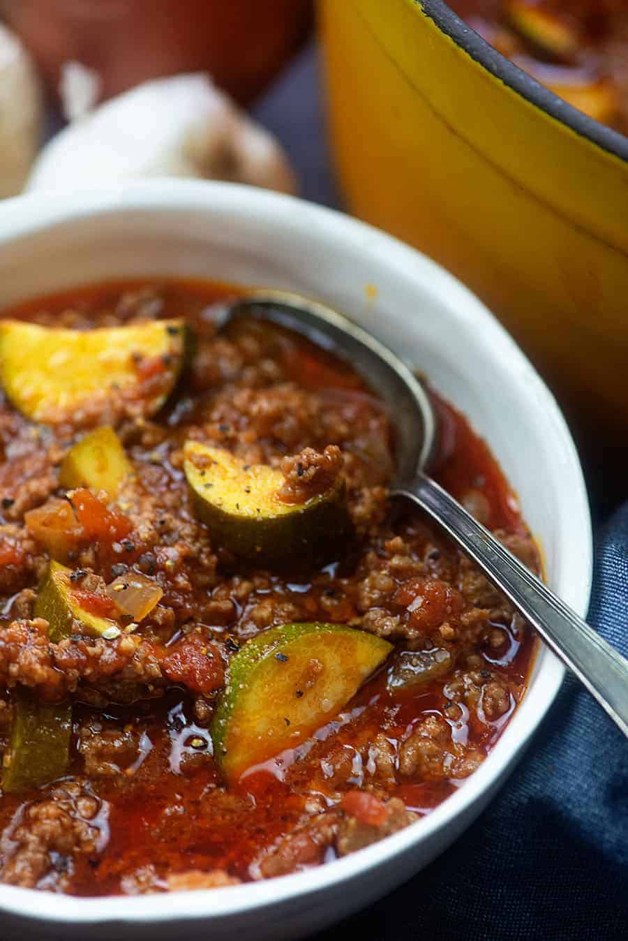 White bowl of goulash with a spoon in it