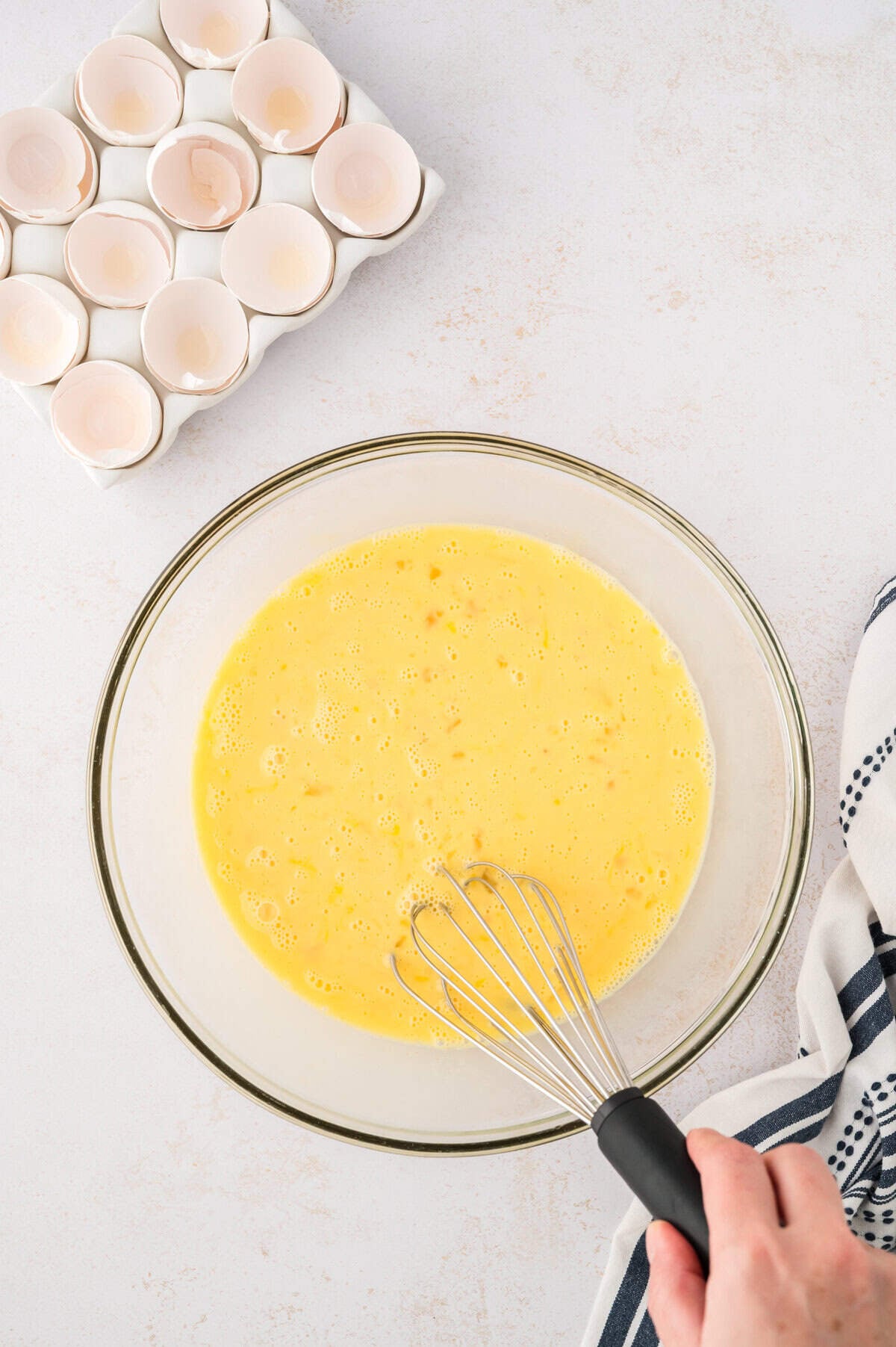 Eggs and milk whisked together in glass bowl.