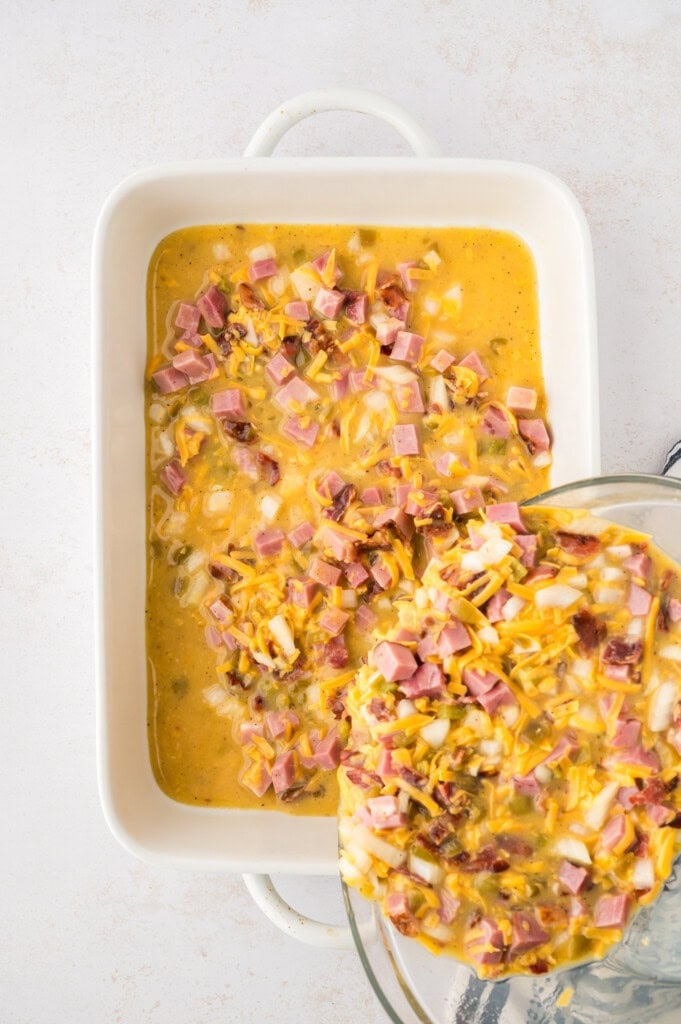 Ingredients for breakfast casserole with ham being poured into 9x13 baking dish.