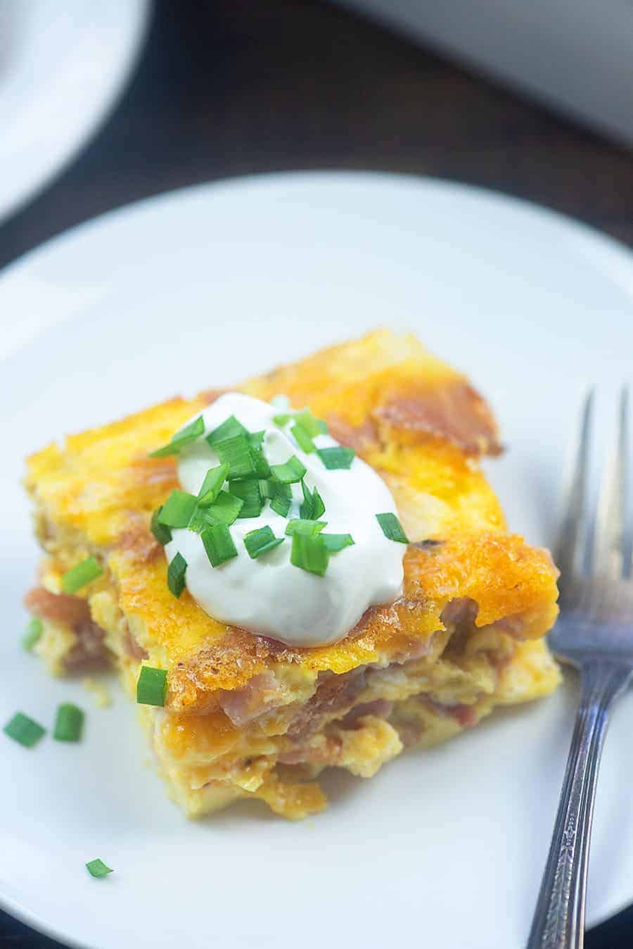 white plate with a piece of breakfast casserole on it topped with chives