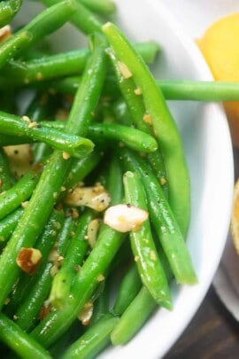 green beans with butter and diced almonds in a white bowl