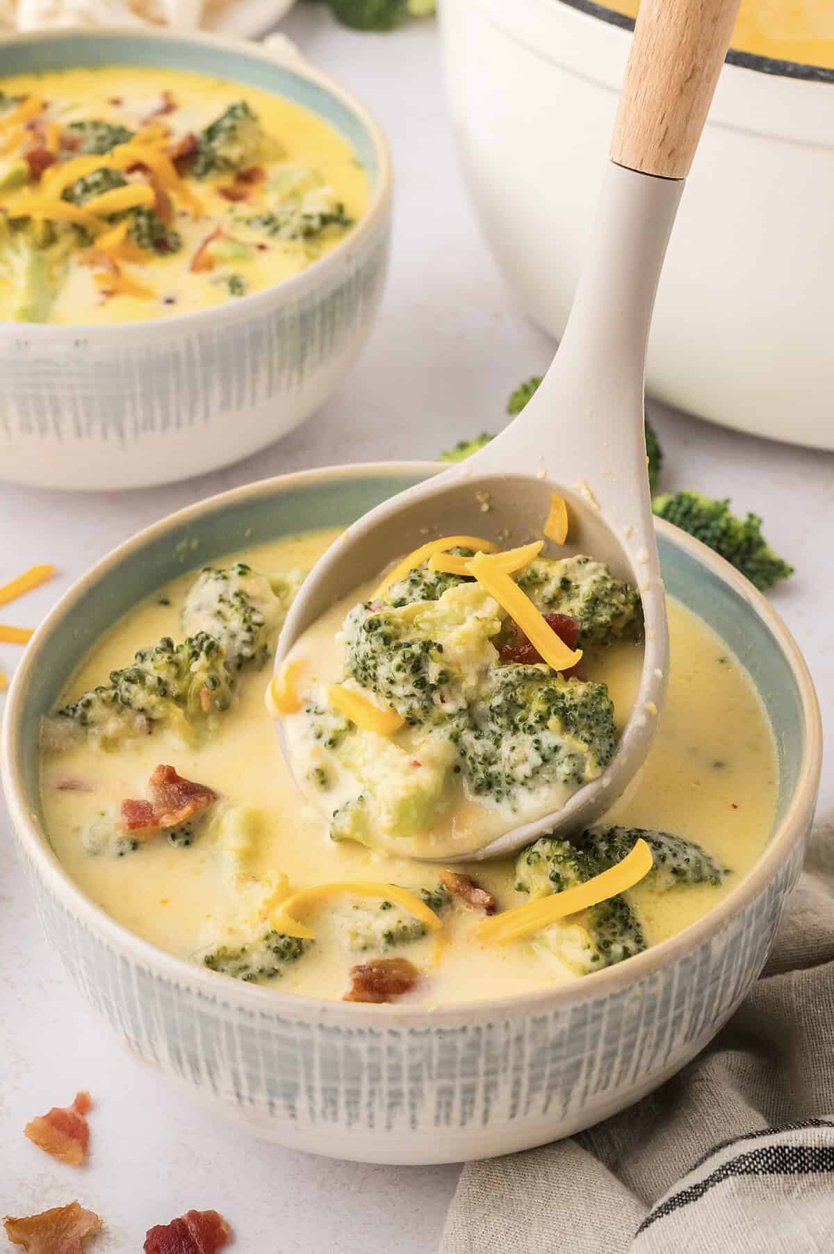 Ladle pouring broccoli cauliflower soup into small bowl.