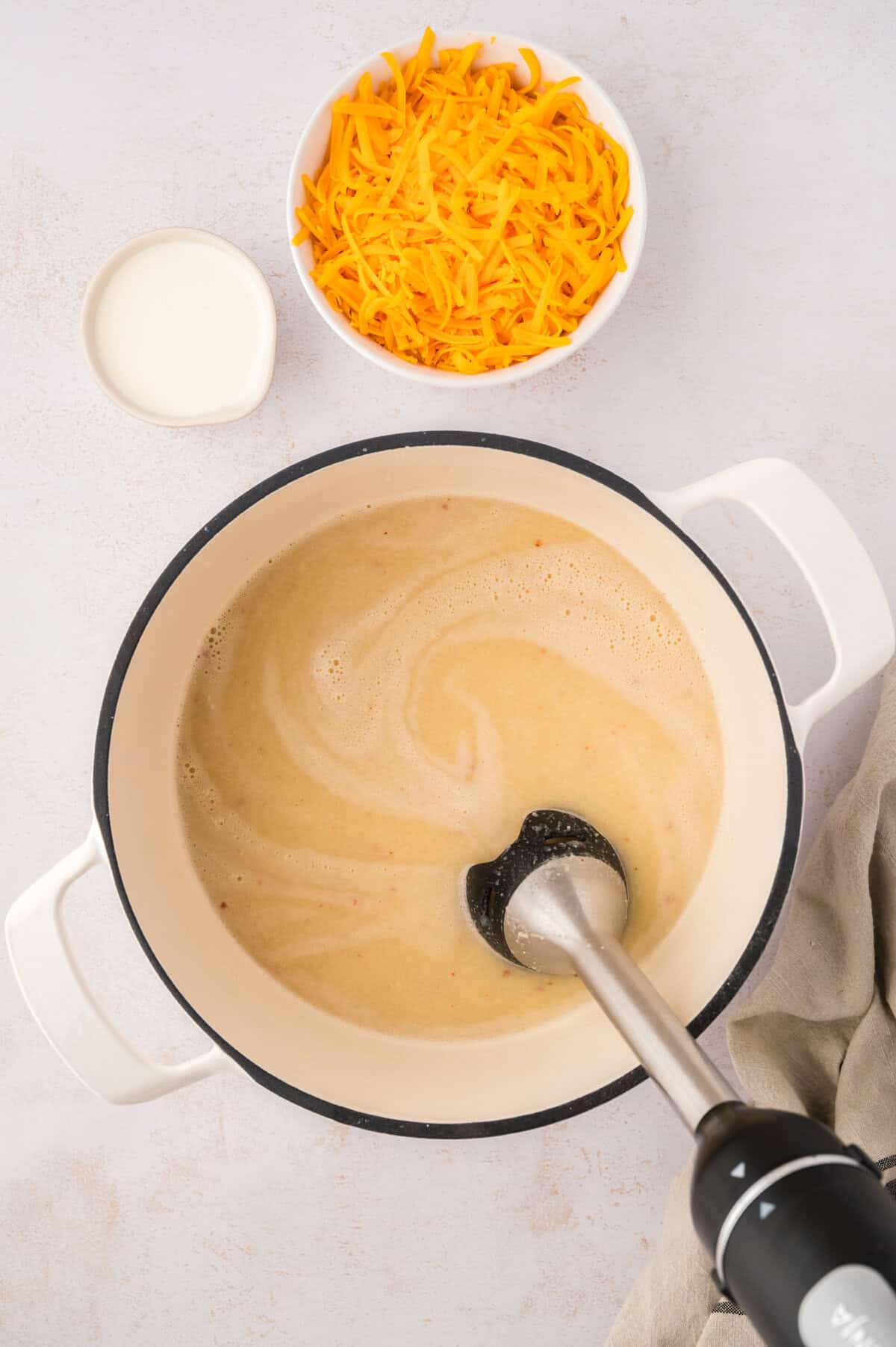 Immersion blender being used to blend up cooked cauliflower in a soup pot.