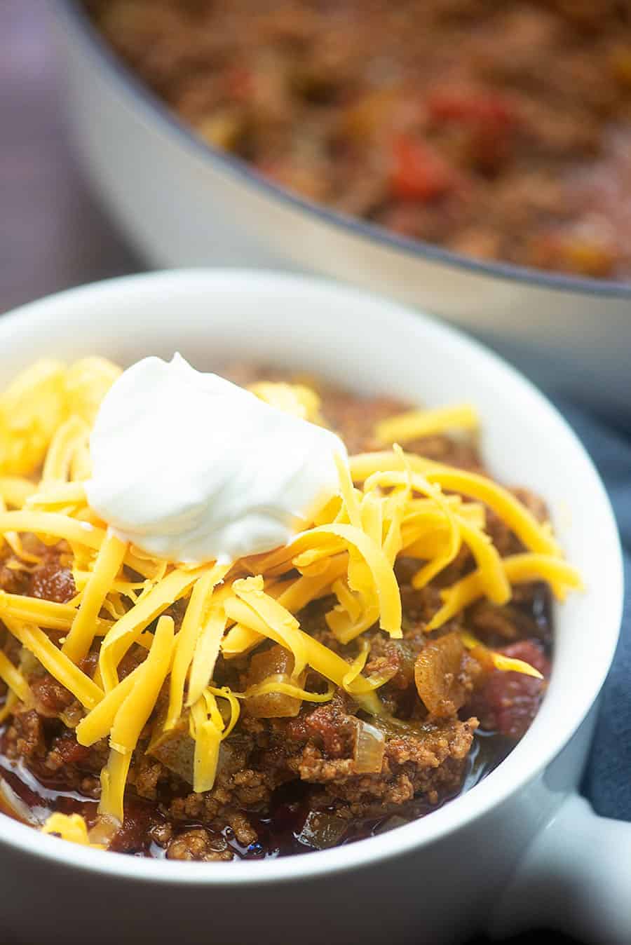 white bowl of chili topped with cheese and a dollop of sour cream