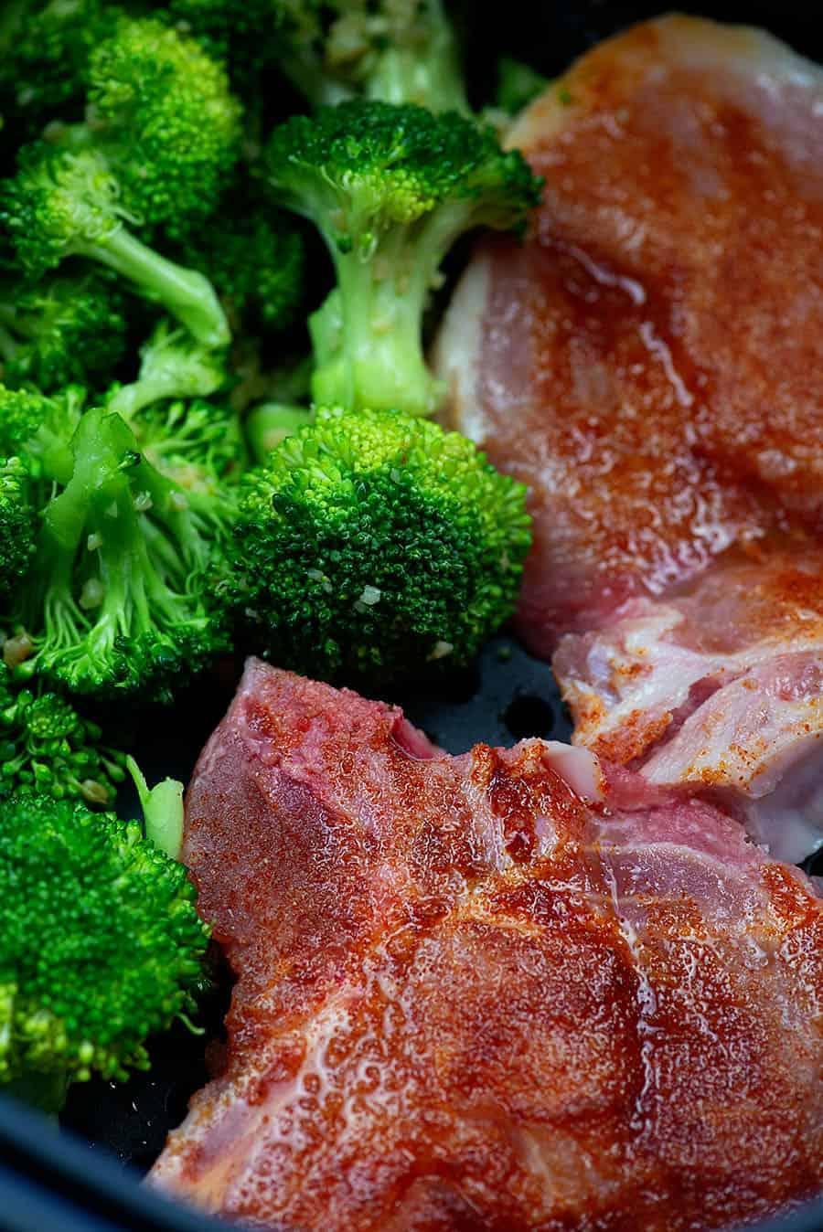 raw pork chops and broccoli in an air fryer basket