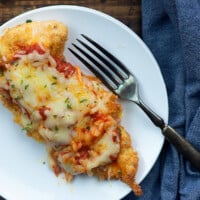 chicken topped with melted cheese and tomato sauce on a white plate with a fork